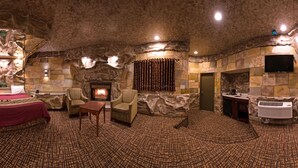 A room with a stone wall fireplace, a large bed with a red cover, a sitting area with a table, and a television mounted on the wall. - Inn of the Dove Romantic Suites with Jetted Tub & Fireplace (Bensalem)