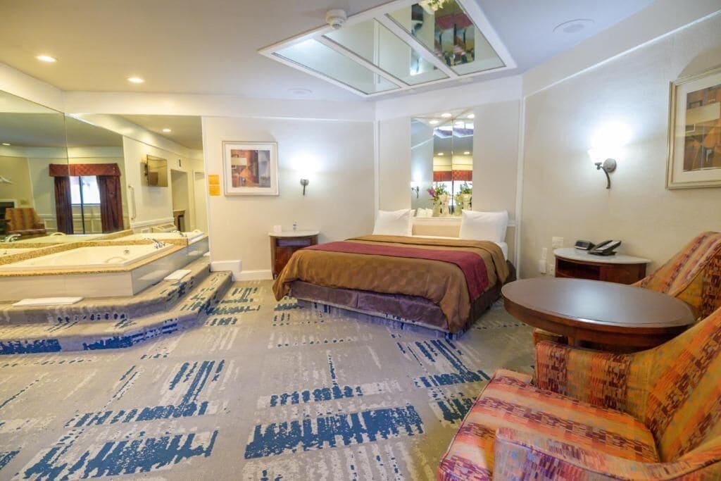 A hotel room with a large bed, a sitting area with a sofa, a small round table, a large mirror, and a ceiling light.