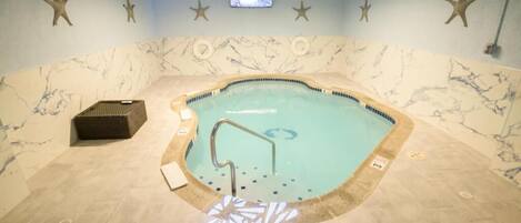 Un jacuzzi con diseño de pared de mármol, un televisor montado en el techo y decoraciones de estrella de mar en la pared.