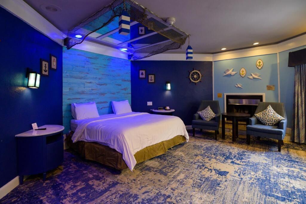 A room with a bed, two side tables, a chair, a small table, and a wall with nautical decorations.