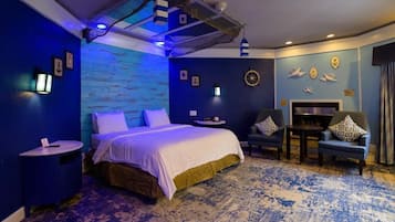 A room with a bed, two side tables, a chair, a small table, and a wall with nautical decorations.