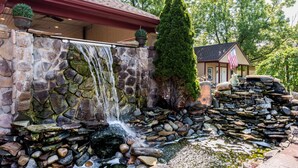 A stone waterfall feature with a small pool at the base, surrounded by a stone wall and a potted plant. - Inn of the Dove Romantic Suites with Jetted Tub & Fireplace (Bensalem)