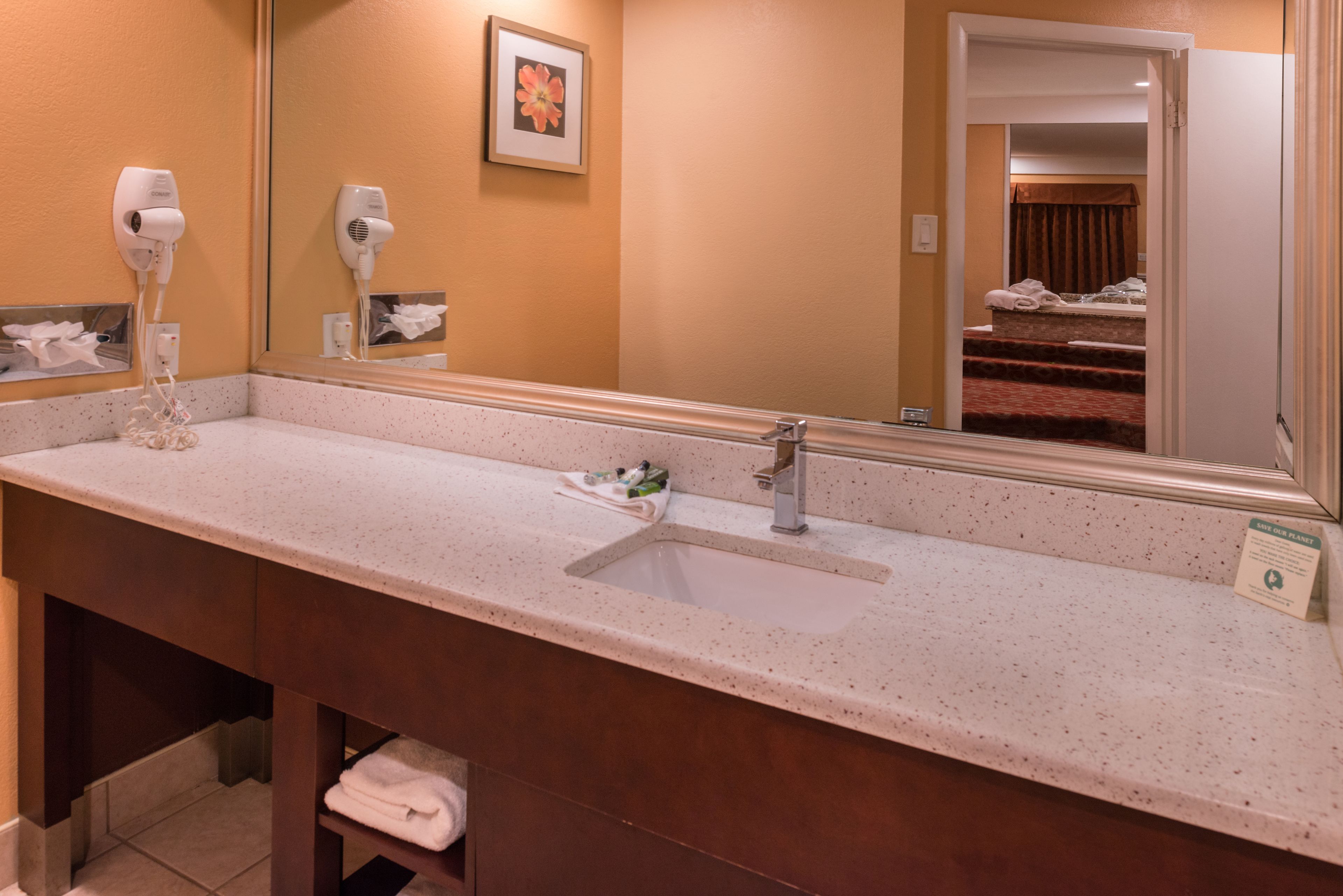 A hotel bathroom with a long countertop, two hair dryers, a sink, and a mirror.