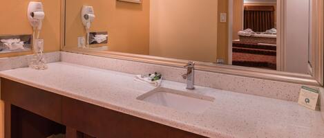 A hotel bathroom with a long countertop, two hair dryers, a sink, and a mirror.