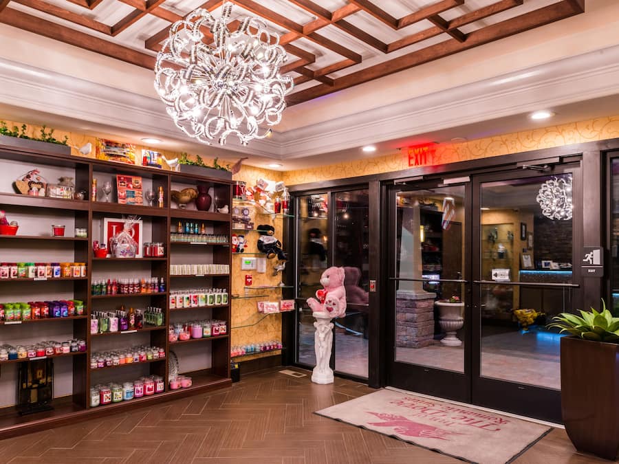 A hotel lobby with a large teddy bear statue, shelves stocked with various items, and a chandelier.