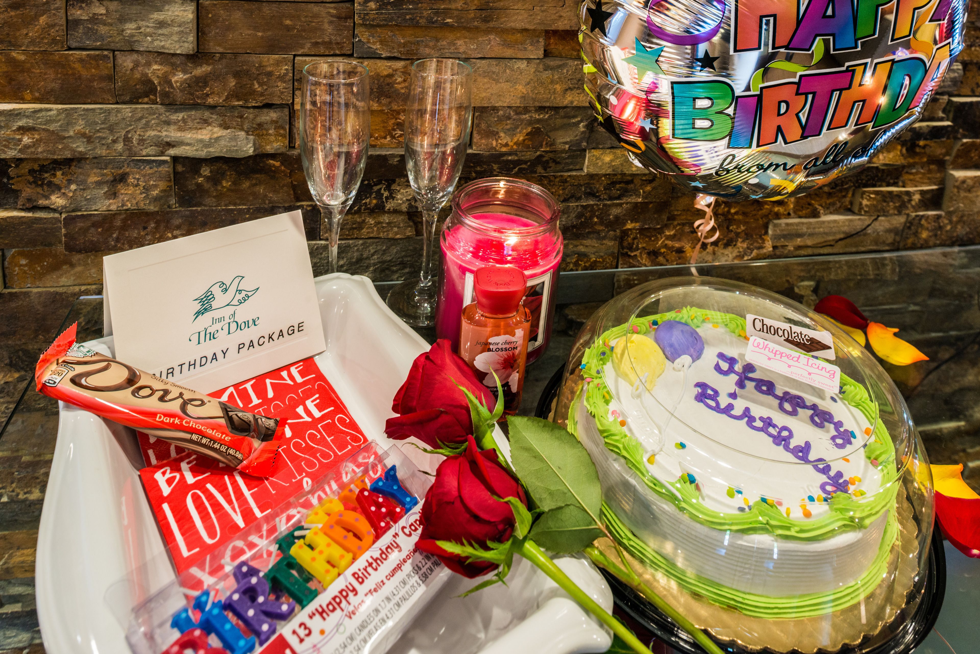 Une table décorée pour un anniversaire, avec un gâteau, une rose, une bougie et une carte de vœux.
