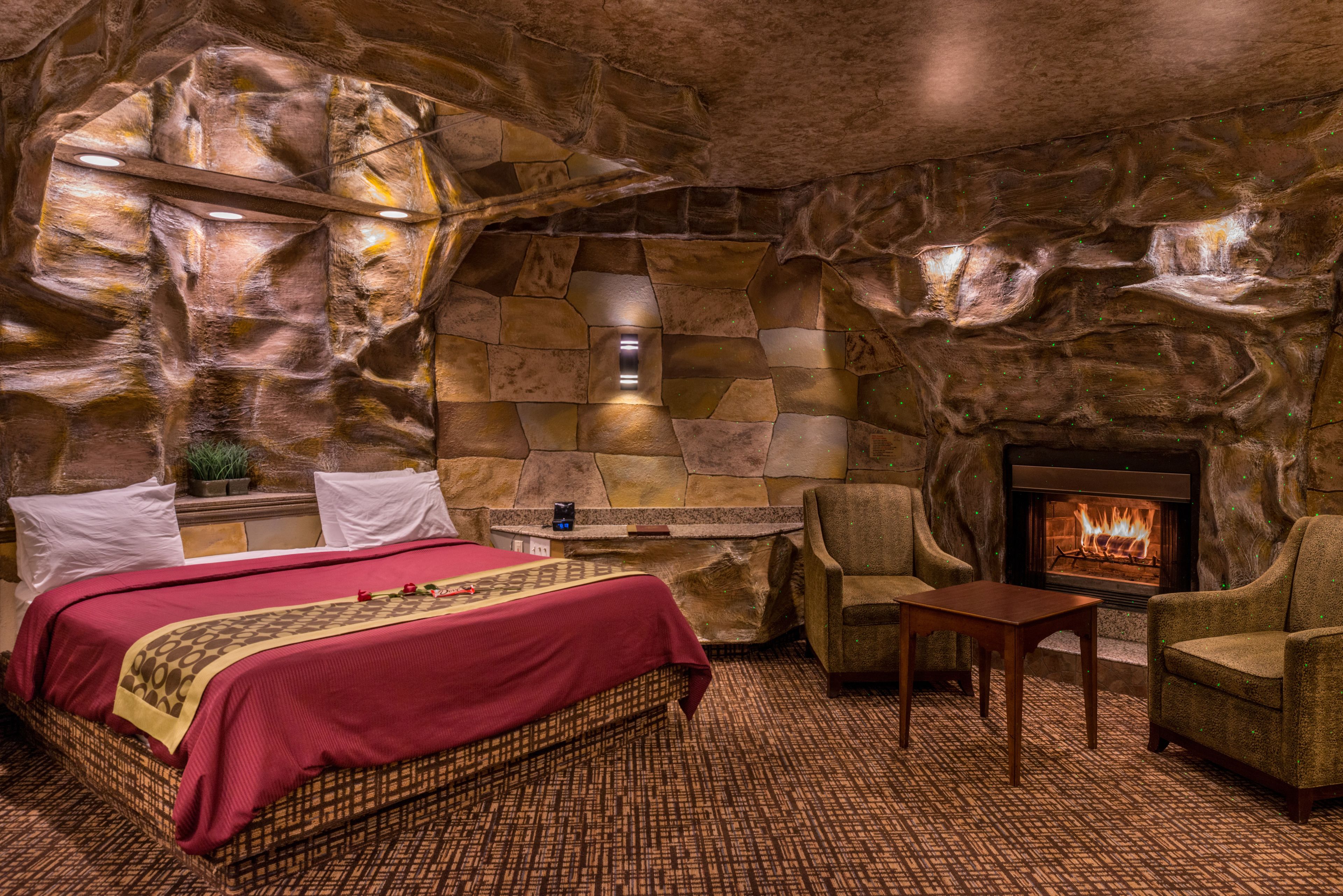 A room with a stone wall, a bed, a fireplace, and two armchairs.