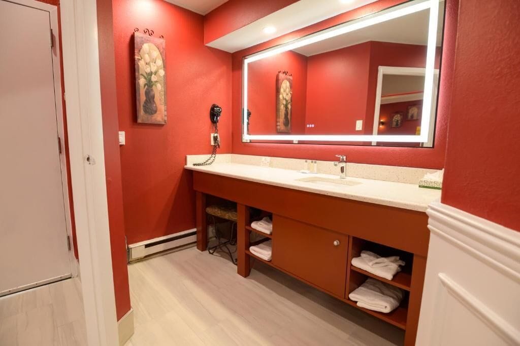 A bathroom with a red wall, a white sink, a mirror, and a towel rack.