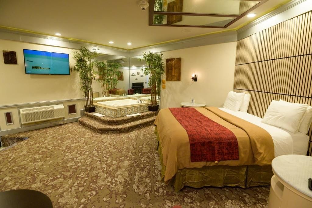 A hotel room with a large bed, a TV, a mirror, and a small sitting area.