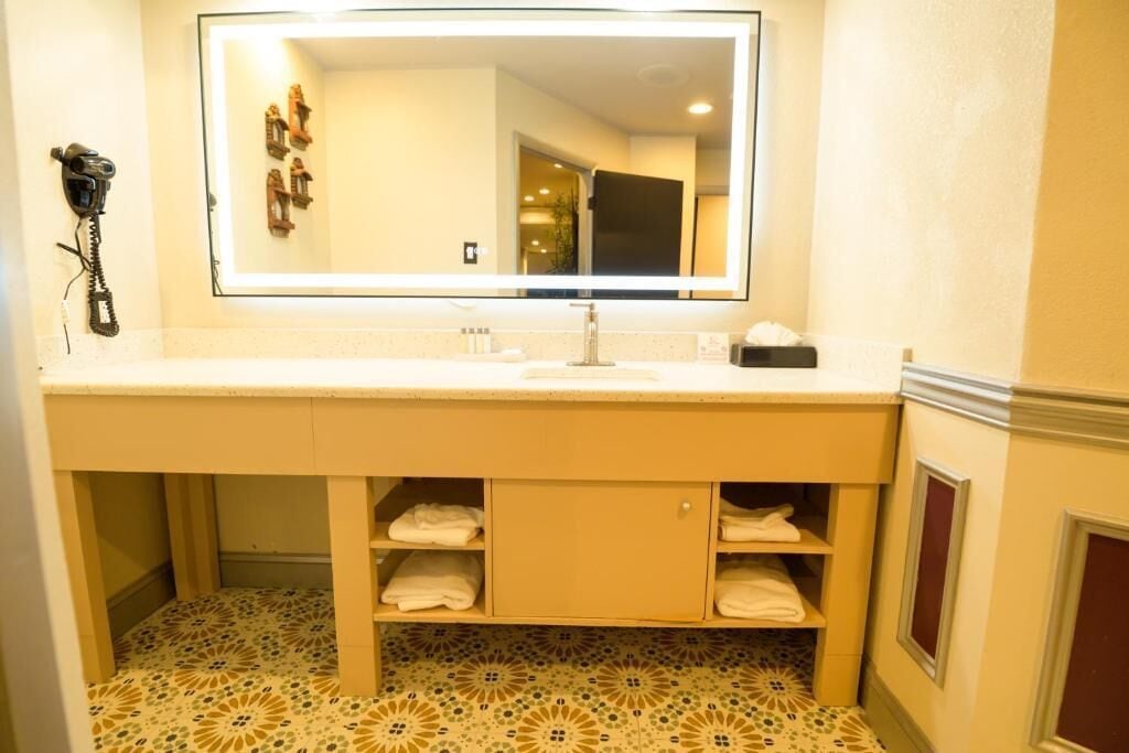 A bathroom with a large mirror, a sink, and shelves under the counter.
