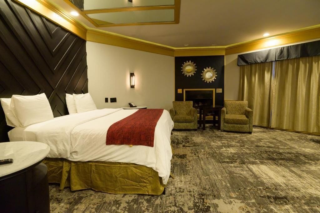 A hotel room with a large bed, a desk, two armchairs, a fireplace, and a view of the outdoors.