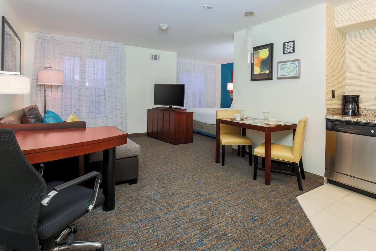 A hotel room with a dining area, a TV, a desk, and a kitchenette.