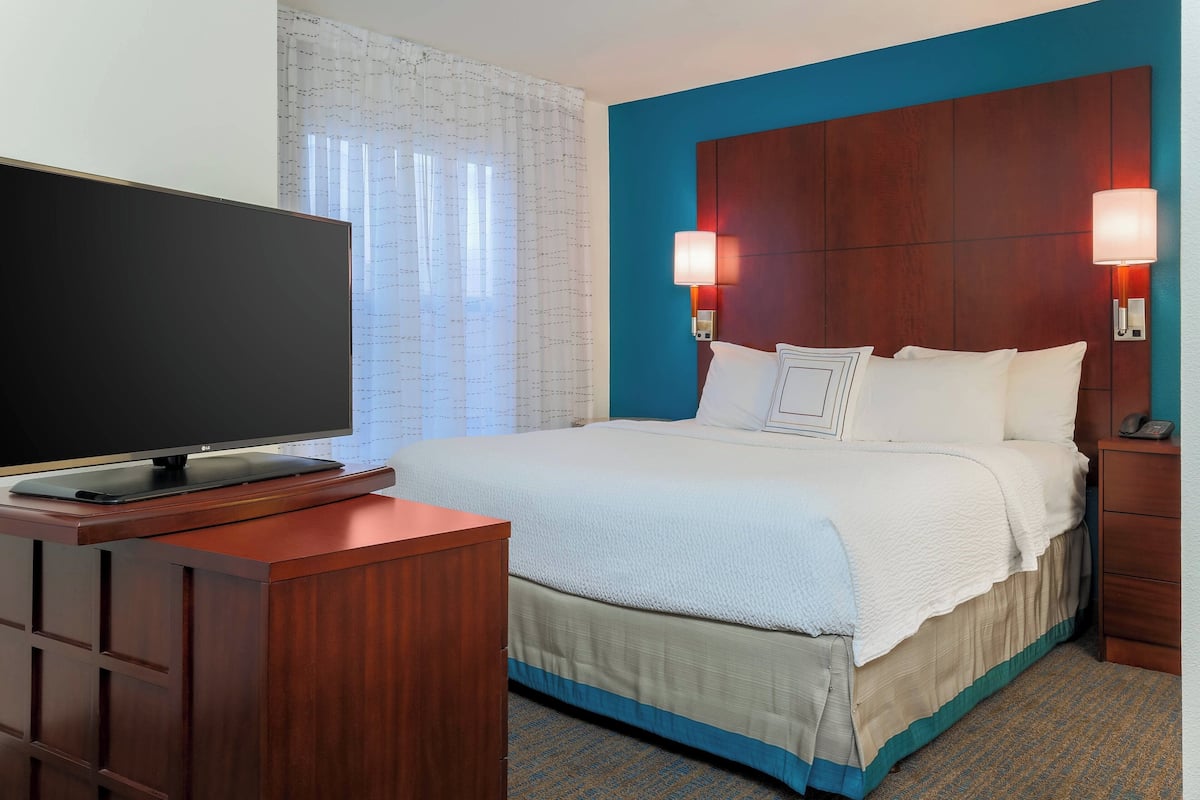 A hotel room with a bed, a TV on a wooden stand, and two wall-mounted lamps.