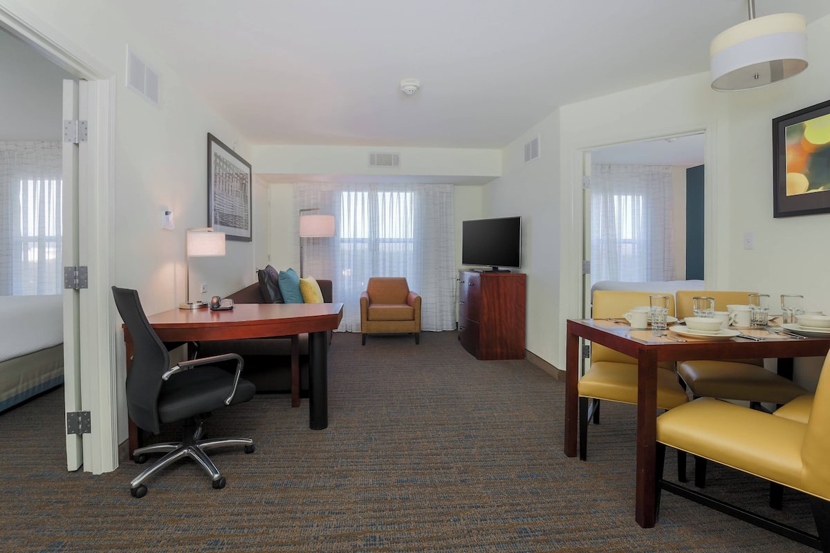 A hotel room with a dining area, a TV, and a window with curtains.