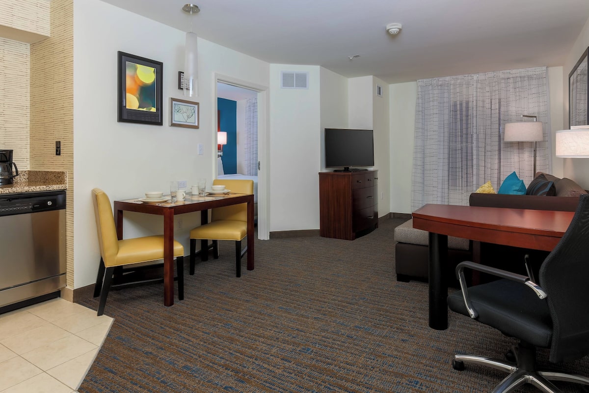 A hotel room with a dining area, a TV, a sofa, and a lamp.