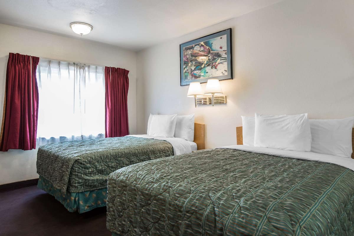 A hotel room with two beds, a painting on the wall, and a window with curtains.