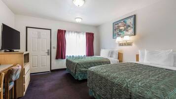 Una camera d'albergo con due letti, una scrivania, una televisione e un quadro appeso al muro.