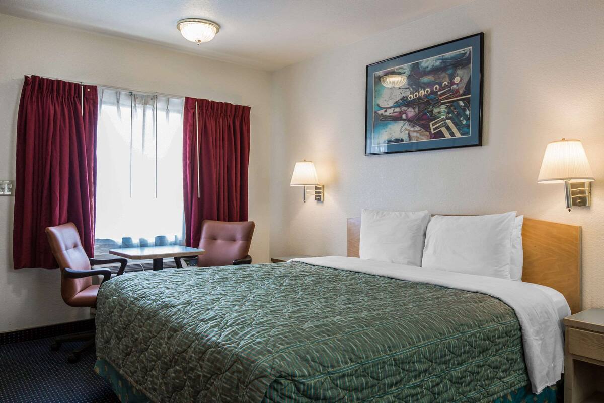 A hotel room with a large bed, two chairs, a table, and two wall-mounted lamps.