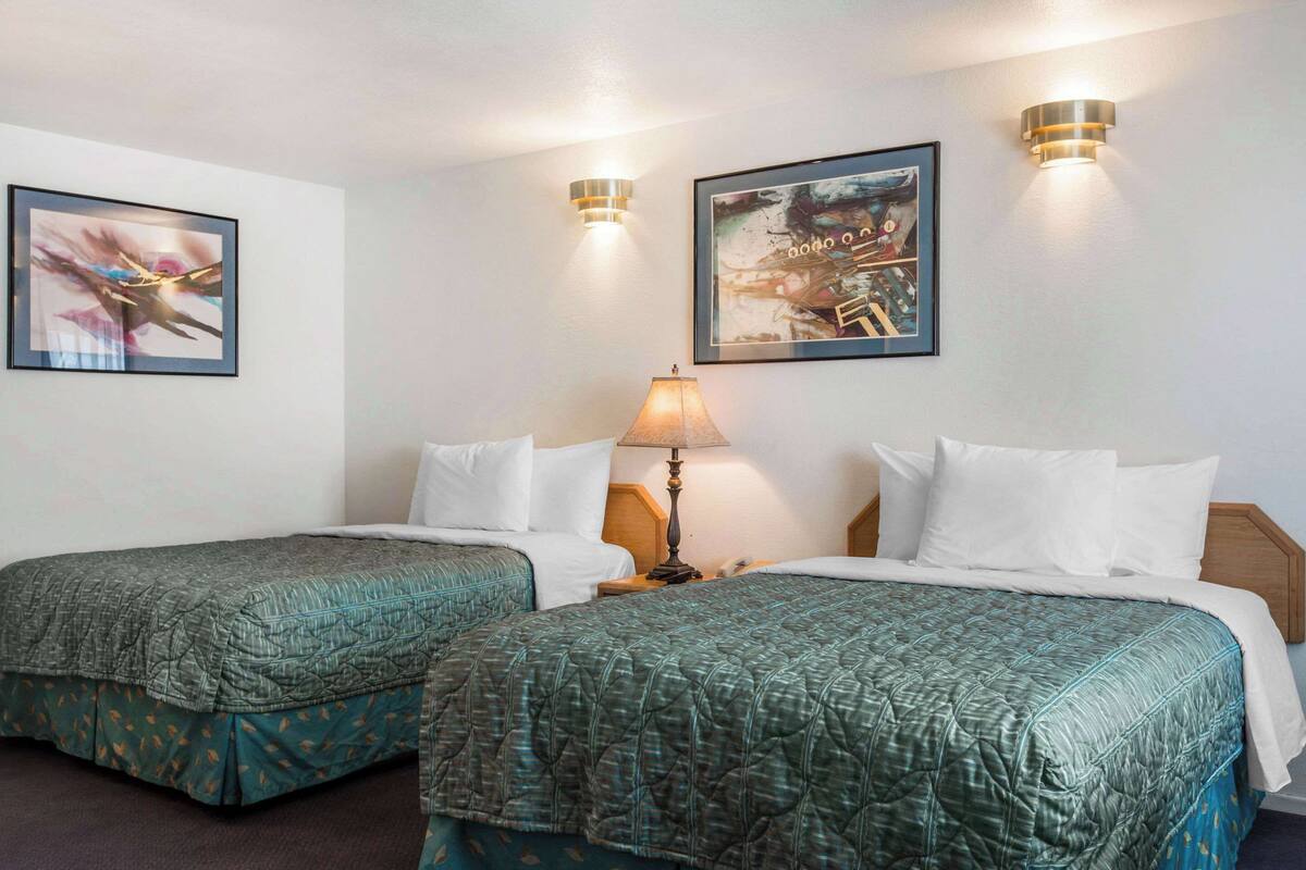 A hotel room with two single beds, a nightstand with a lamp, and two wall-mounted light fixtures.
