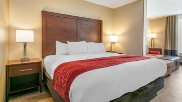 A hotel room with a large bed, two bedside tables with lamps, a nightstand, a red throw blanket, and a view of the outdoors.