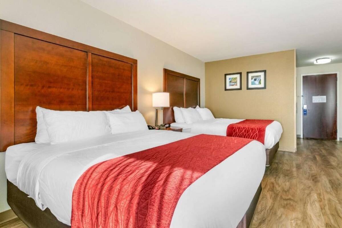 A hotel room with two beds, a wooden headboard, a nightstand with a lamp, and a door with a sign.