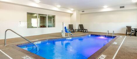 An indoor swimming pool with clear lane markings, a changing room, and a seating area with chairs.