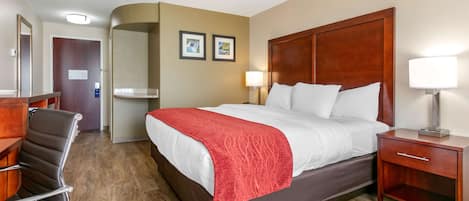 Una habitación de hotel con cama, escritorio, silla, mesita de noche y lámpara.