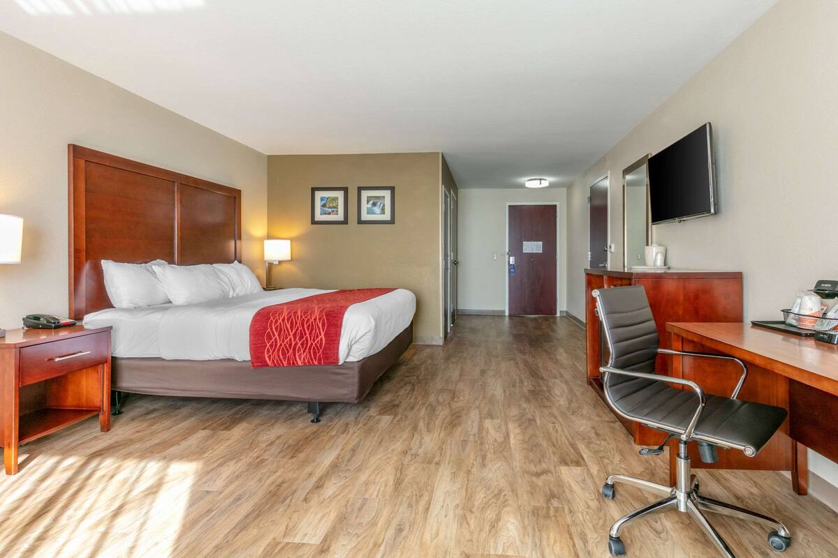 A hotel room with a bed, desk, chair, and a TV mounted on the wall.