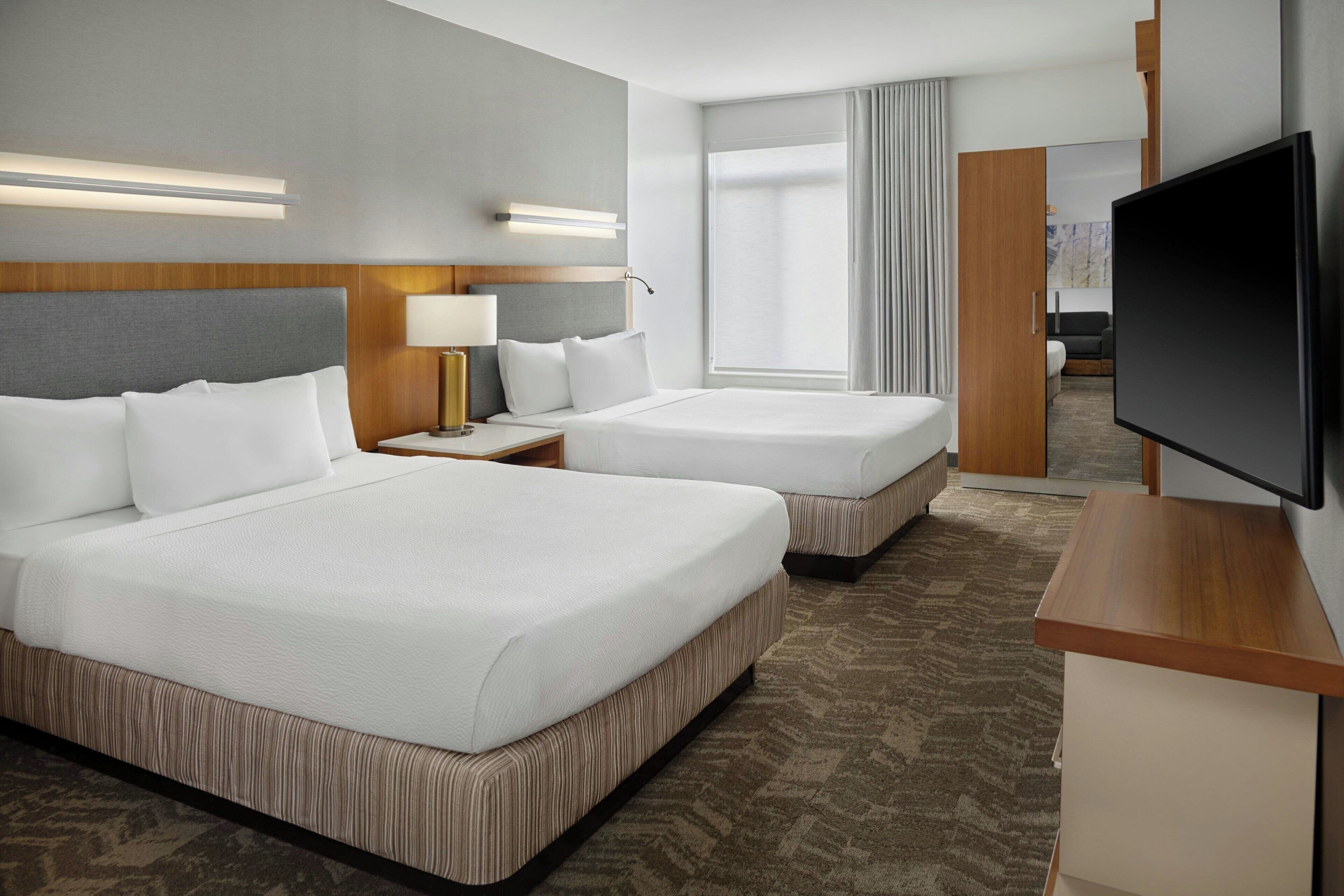 A hotel room with two beds, a TV, a desk, and a large window.
