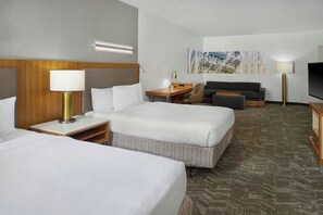 A hotel room with two beds, a desk, a sofa, a TV, and a painting on the wall.