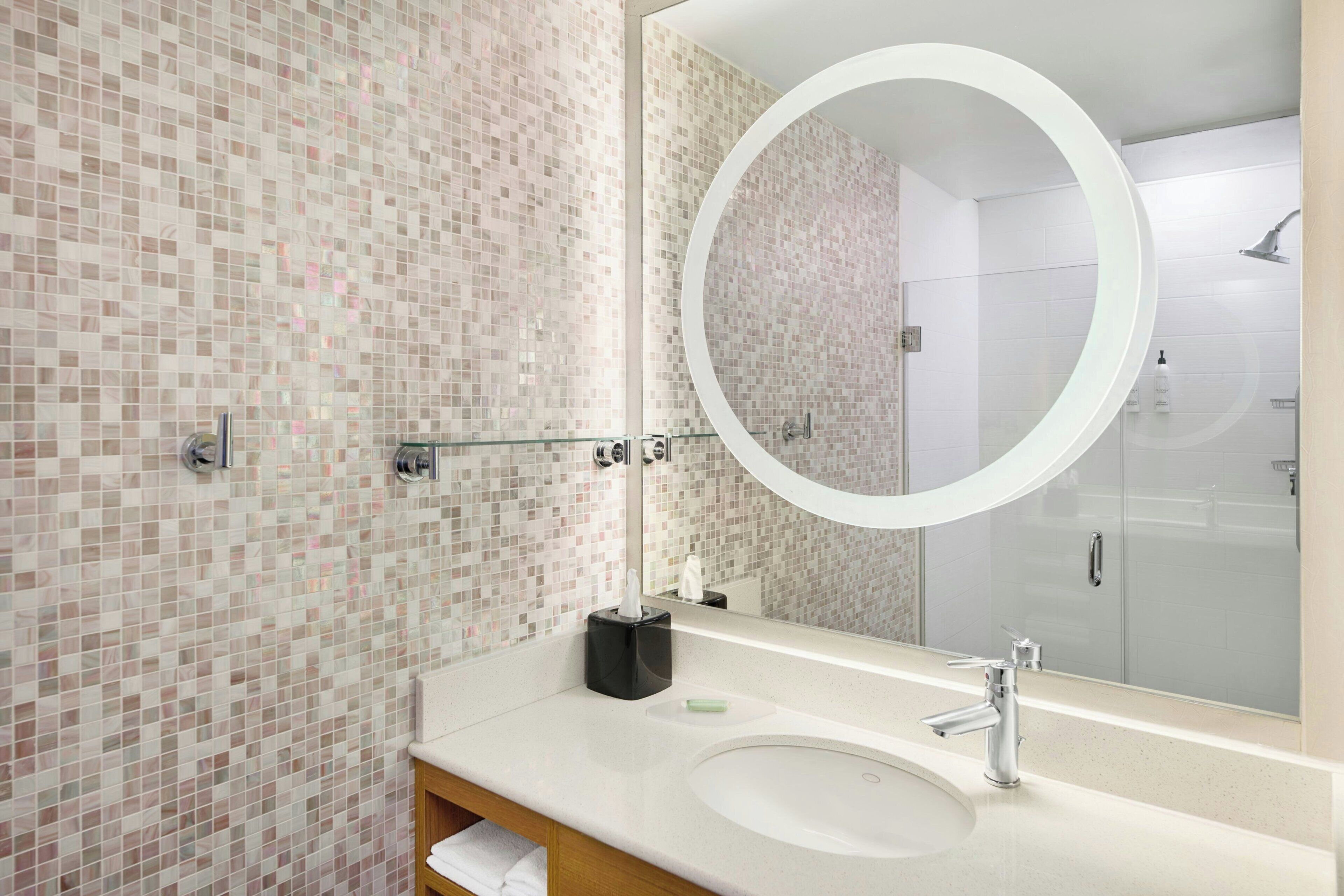 A bathroom with a mosaic tile wall, a round mirror, a sink, and a shower area.