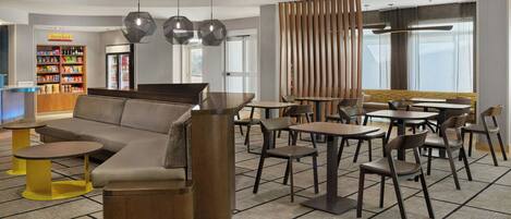 Eine moderne Lounge mit einer Couch, Tischen, Stühlen und einem Automaten.