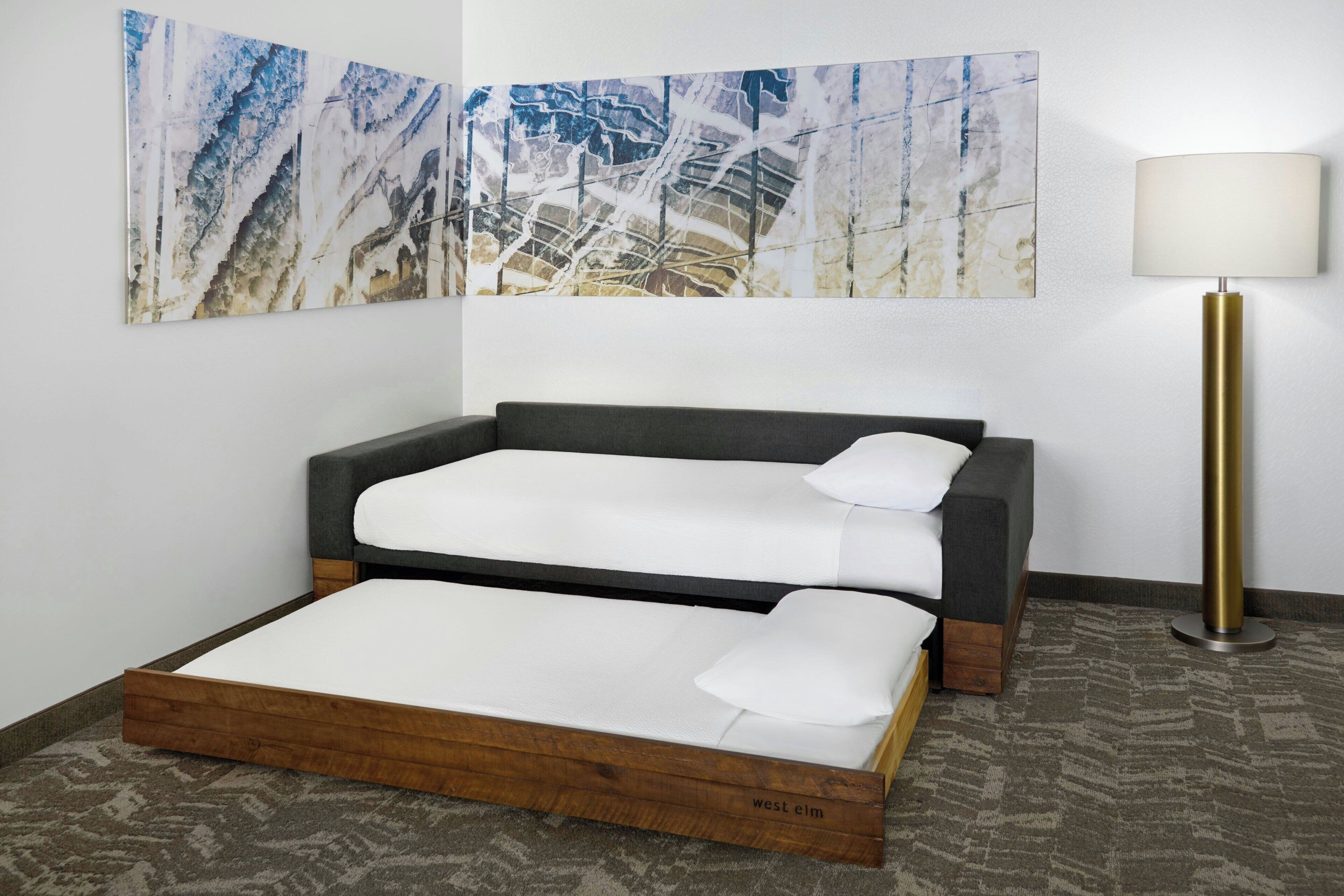 Una habitación con cama, lámpara y un cuadro abstracto grande en la pared.