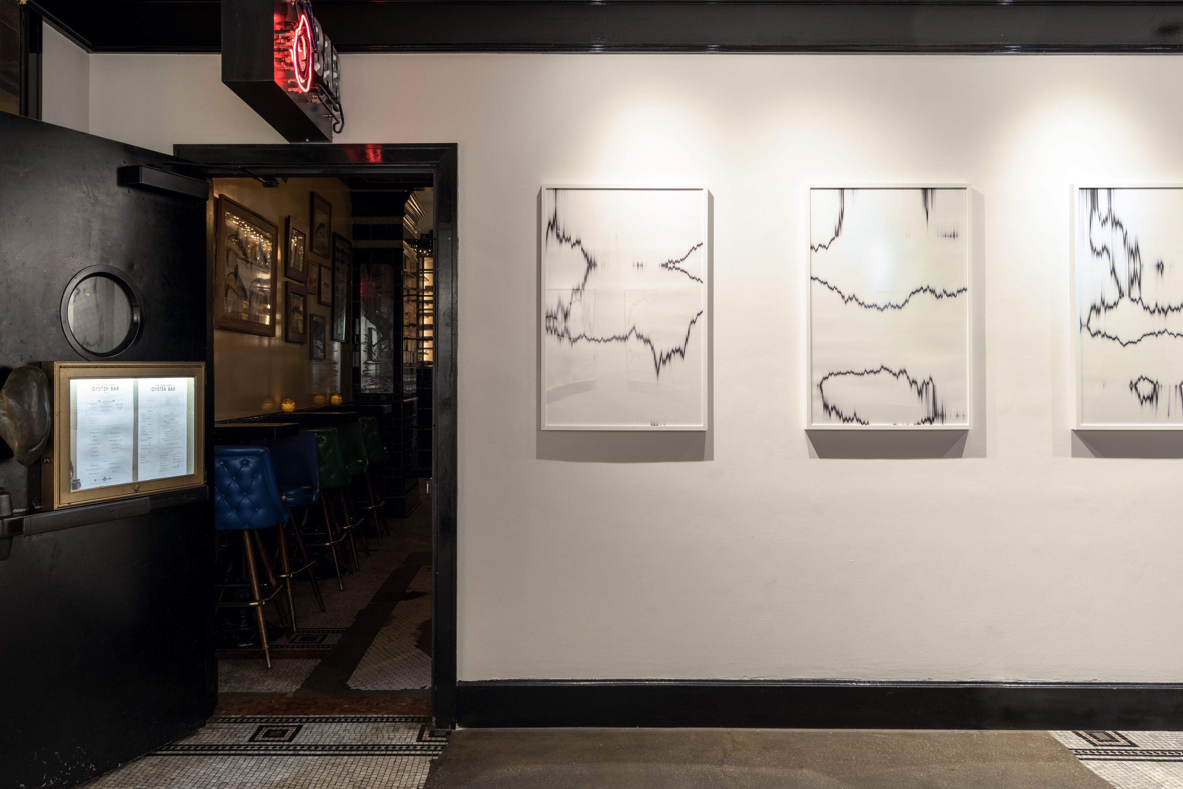 Une galerie d’art où sont exposées, accrochées au mur, des peintures abstraites encadrées.
