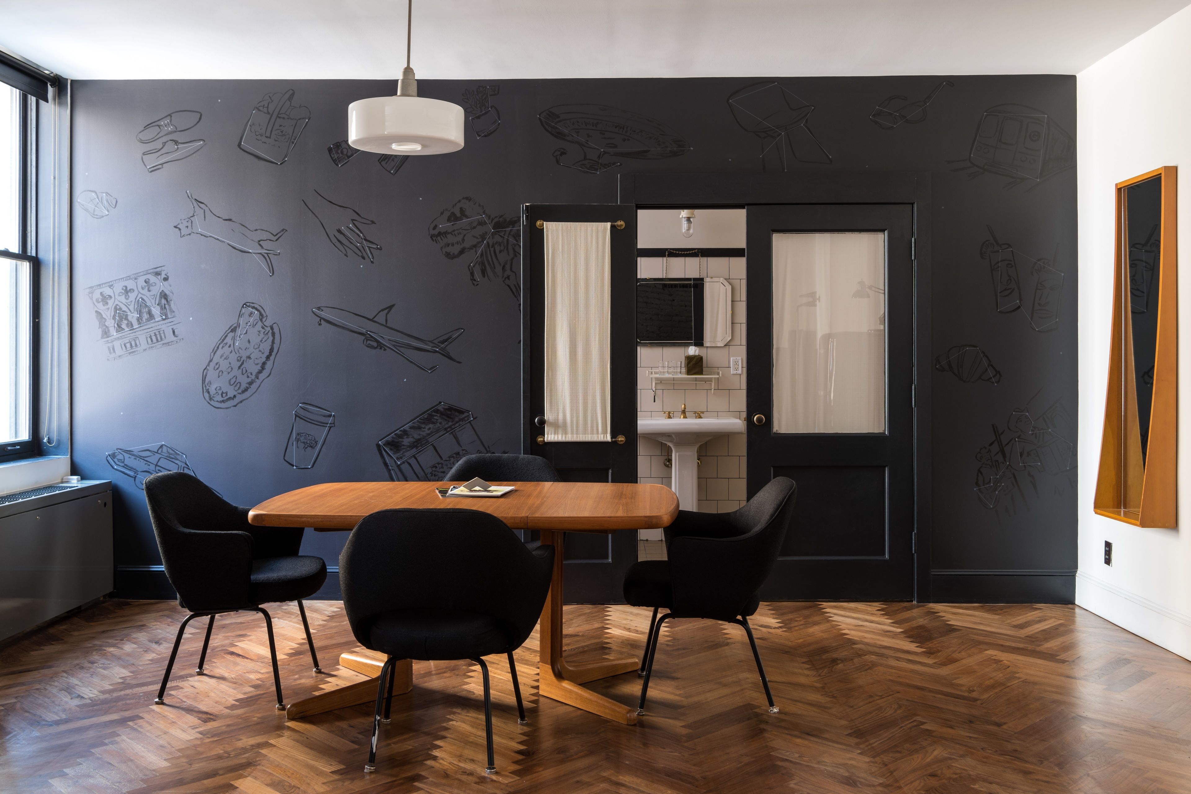 A modern dining area with a wooden table and black chairs, a black and white patterned wall, and a view into the kitchen.
