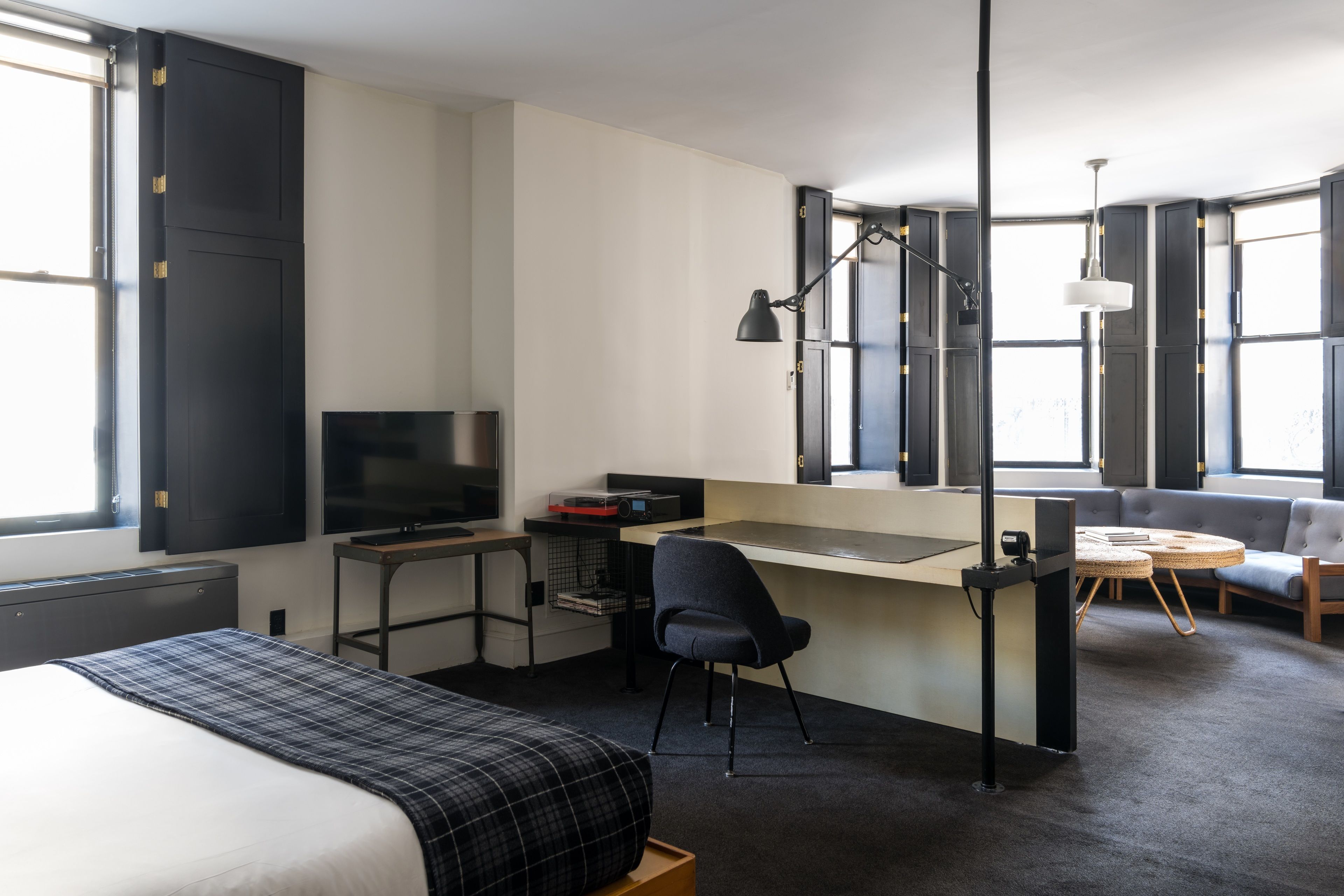 Een moderne hotelkamer met een bed, bureau, stoel, televisie en grote ramen.