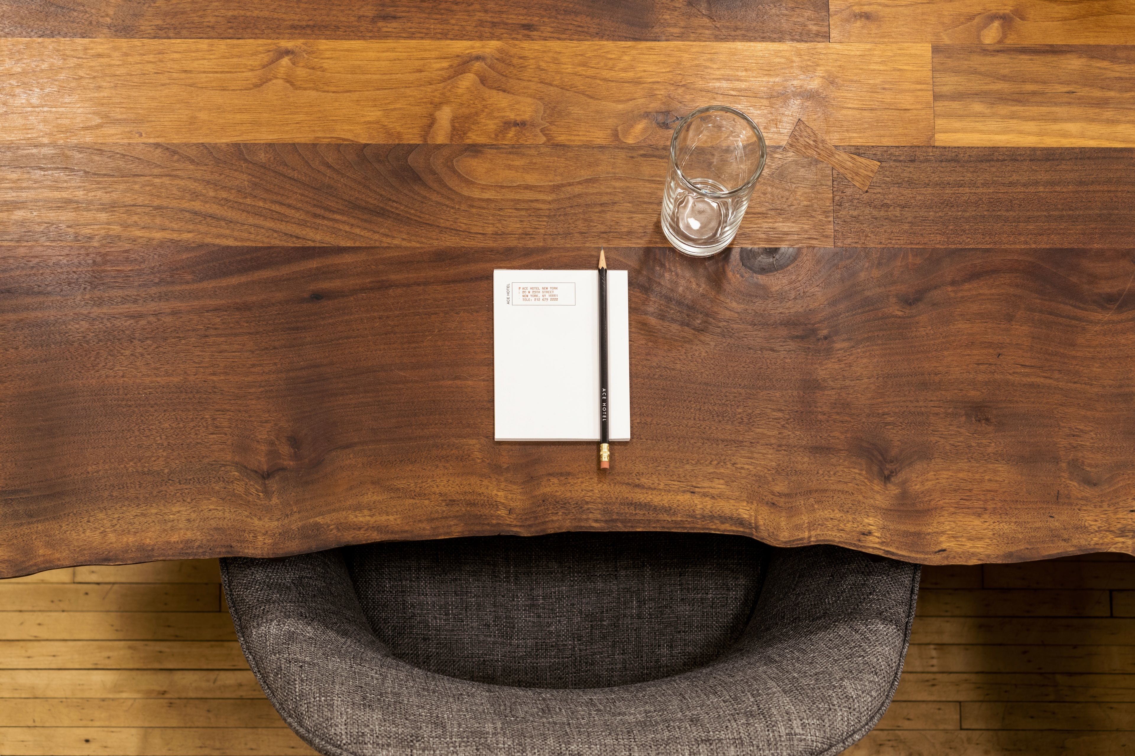 A wooden table with a notebook, pencil, and glass.