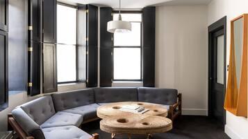 Un salon moderne avec un canapé d’angle gris, une table basse ronde en fibres tressées et un luminaire suspendu.