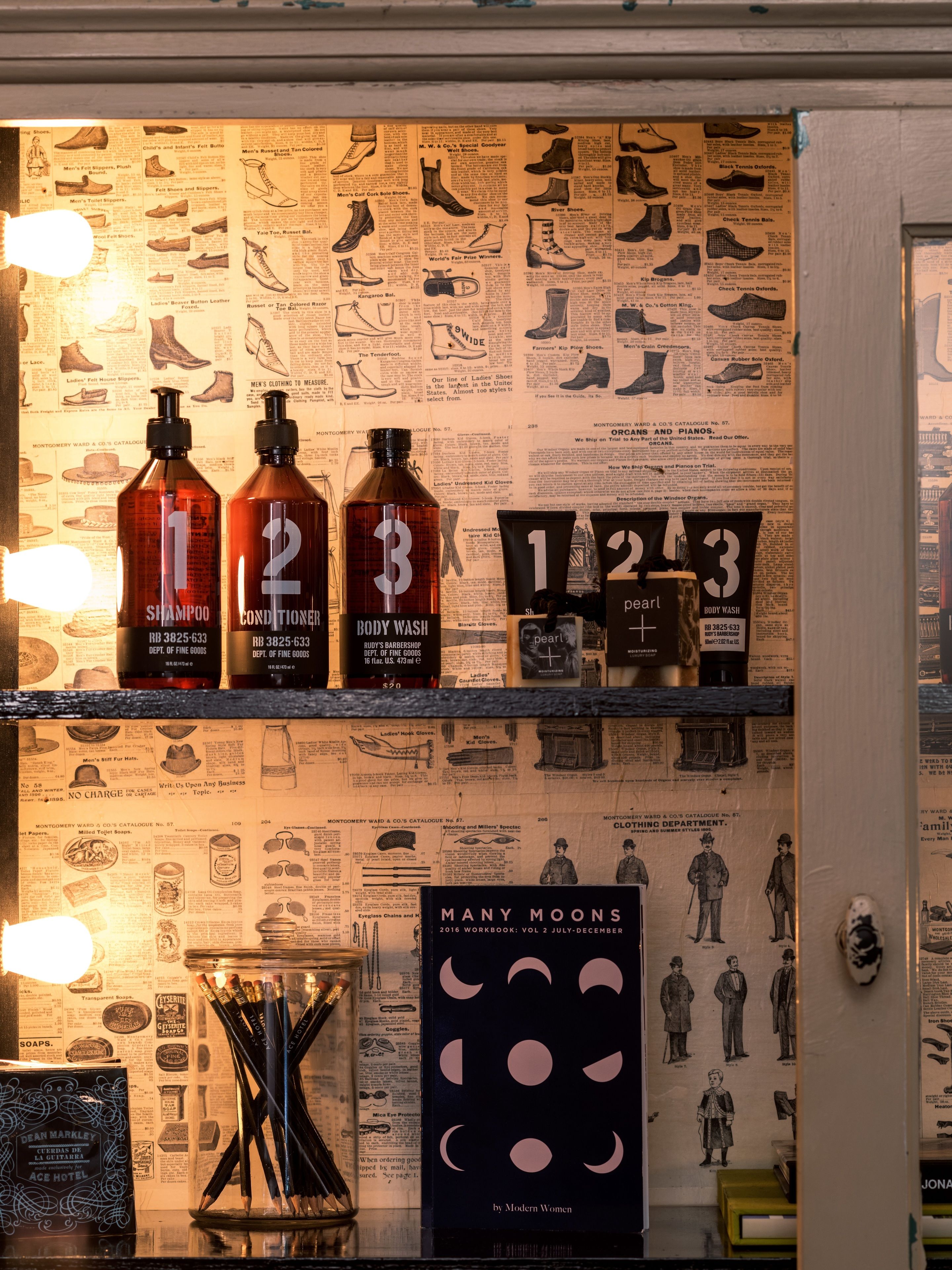 A bathroom with vintage-style decor, including a wall with old advertisements and a mirror. There are three bottles of toiletries on the counter.