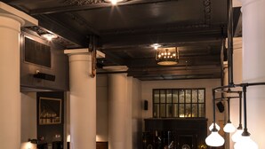En rummelig lobby med høje lofter, detaljeret loftudsmykning og forskellige siddeområder med sofaer og stole.