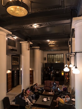 A spacious cafe with high ceilings, exposed ductwork, and pendant lighting. Tables are arranged for groups, with a central seating area featuring leather couches. at Ace Hotel New York