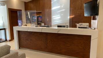 A reception desk with a wooden panel design, a glass partition, and a flat-screen TV mounted on the wall.