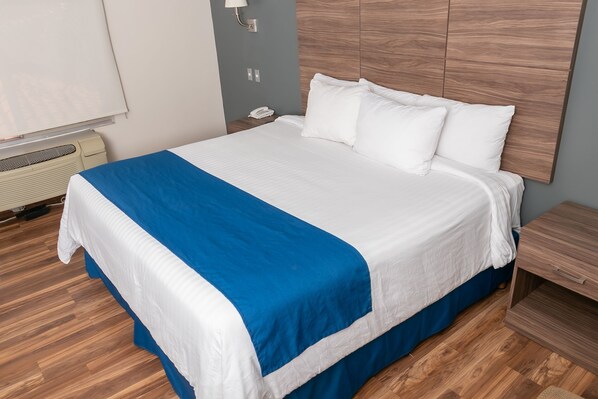 A hotel room with a bed, a nightstand, a phone, and a wall-mounted heater.
