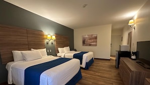 Habitación de hotel con dos camas, cabeceros de madera, un escritorio con televisor y un cuadro en la pared.