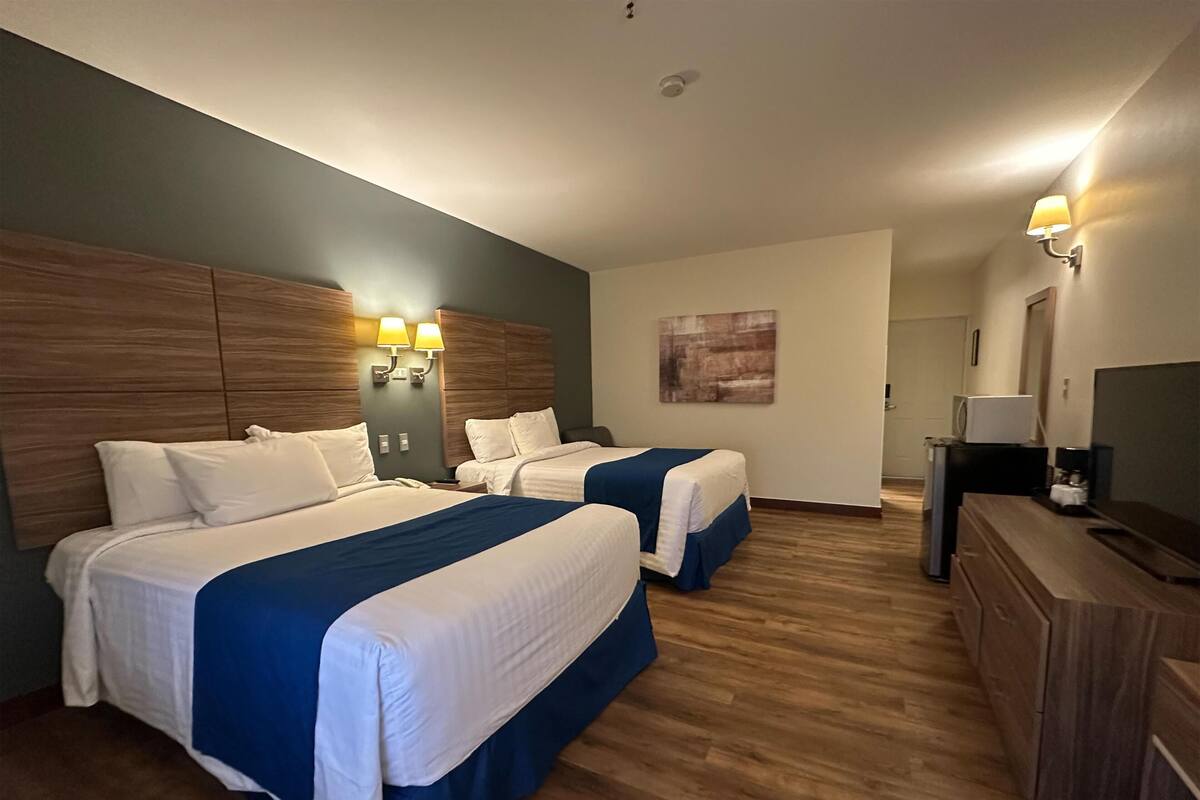 A hotel room with two beds, wooden headboards, a desk with a TV, and a painting on the wall.