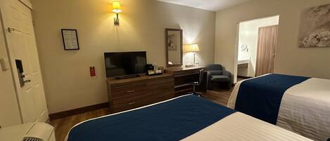 A hotel room with two beds, a desk with a television, a chair, and a lamp.