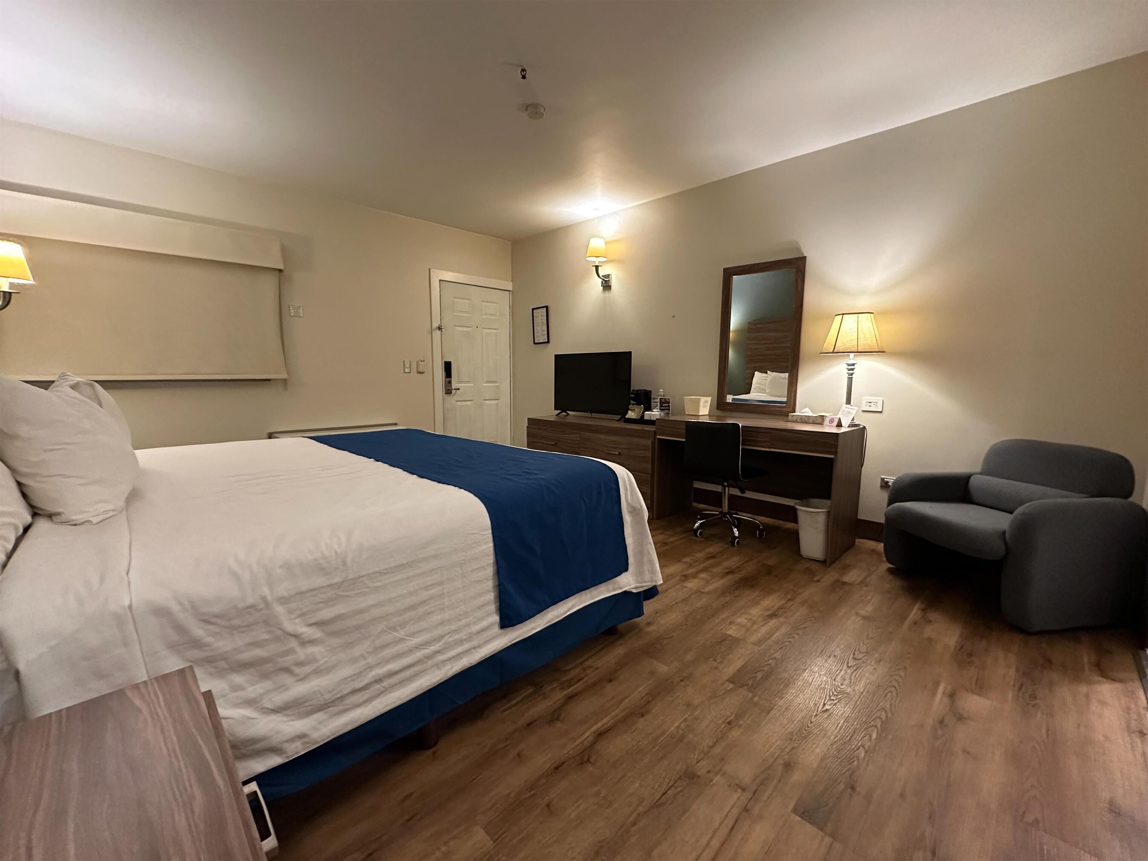 A hotel room with a bed, a desk, a chair, a TV, and a mirror.