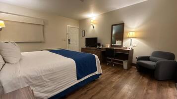 A hotel room with a bed, a desk, a chair, a TV, and a mirror.