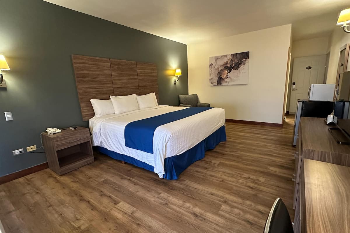 A hotel room with a large bed, wooden headboard, bedside tables, a desk, and a chair.