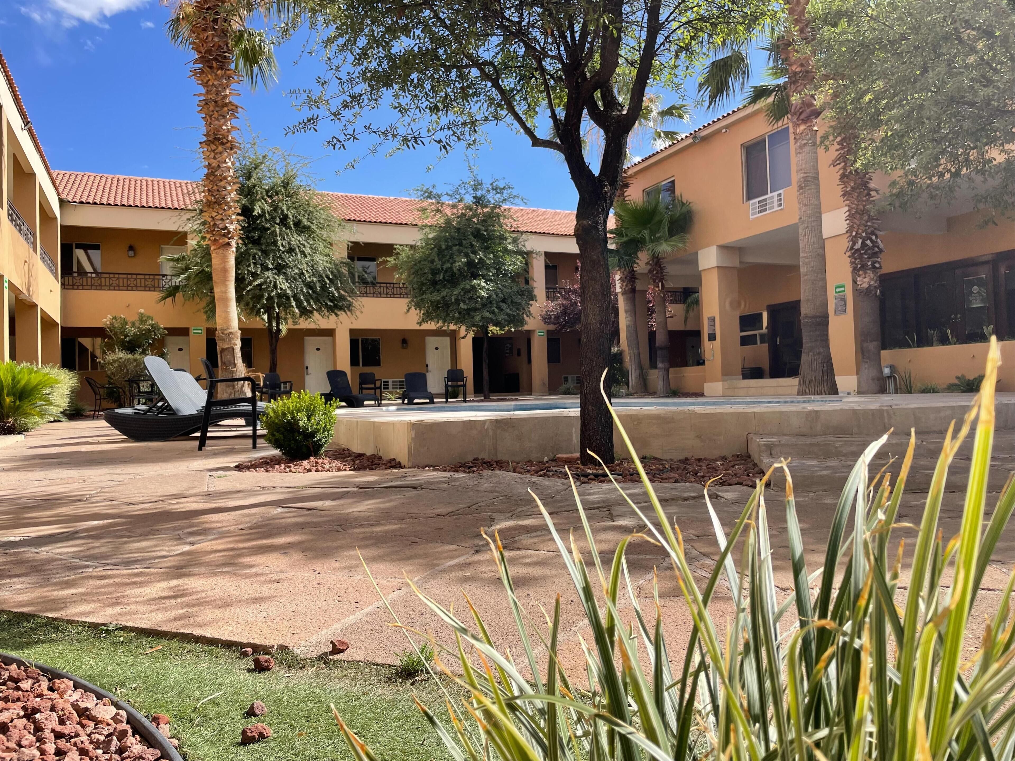 A courtyard with outdoor seating, palm trees, and a building with a red-tiled roof.